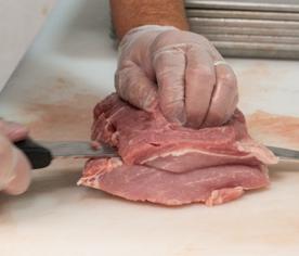 A butcher hand-cutting fresh pork chops at the cutting board