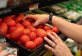 Hands restocking fresh tomatoes in the produce case